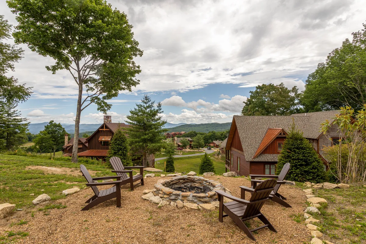 A cozy fire pit surrounded by Adirondack chairs set against distant mountain views and lush trees. The scene invites guests to gather for storytelling, stargazing, and relaxing evenings in a communal outdoor space.