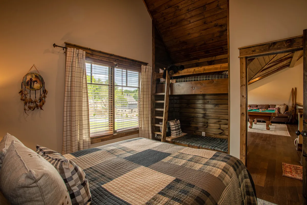 A family-friendly bedroom with a plaid quilt on the bed, a wooden lofted bunk, and large windows letting in ample natural light. The design is both cozy and playful.