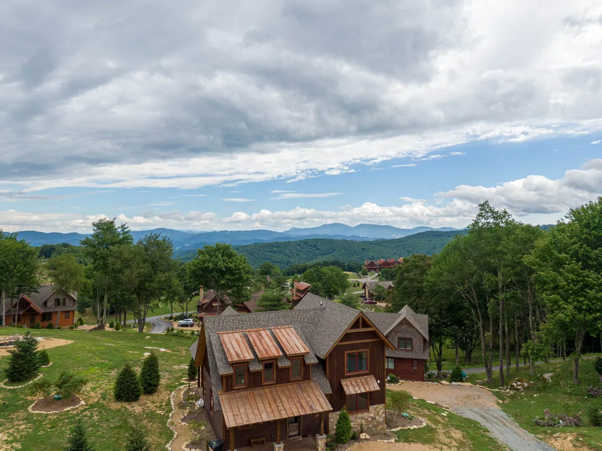 A tranquil exterior shot highlighting the wooden cabin nestled amongst lush greenery, set before a dramatic mountain range. The setting suggests hiking, nature walks, and peaceful moments in the outdoors with family.