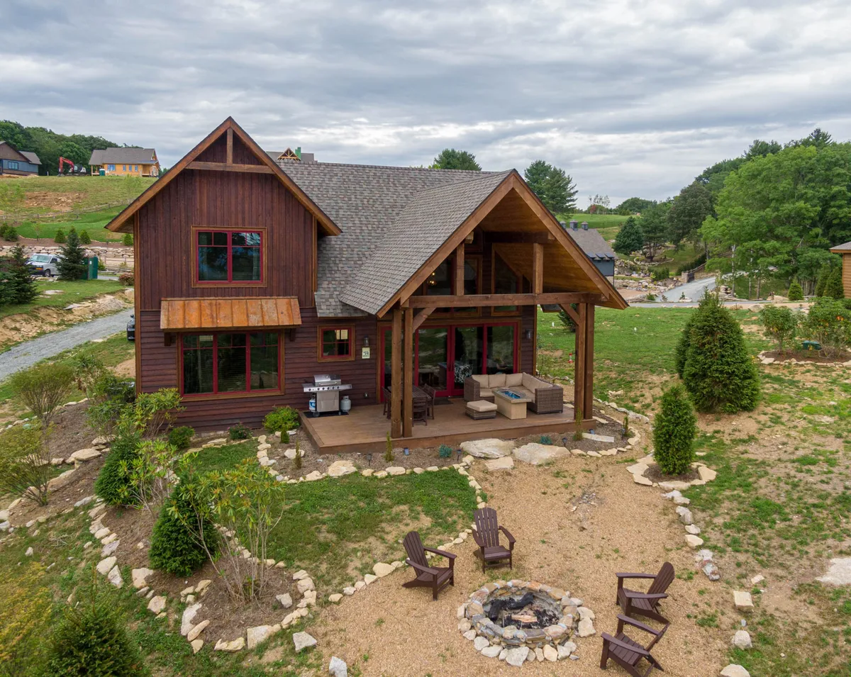 This exterior image showcases the wooden cabin with a welcoming outdoor seating area and a fire pit surrounded by a landscaped garden. The porch appears spacious and inviting, offering plenty of room to relax while taking in the mountain air. The overall setting is cozy and perfect for hosting outdoor gatherings, relaxing with friends and family, or simply enjoying nature.