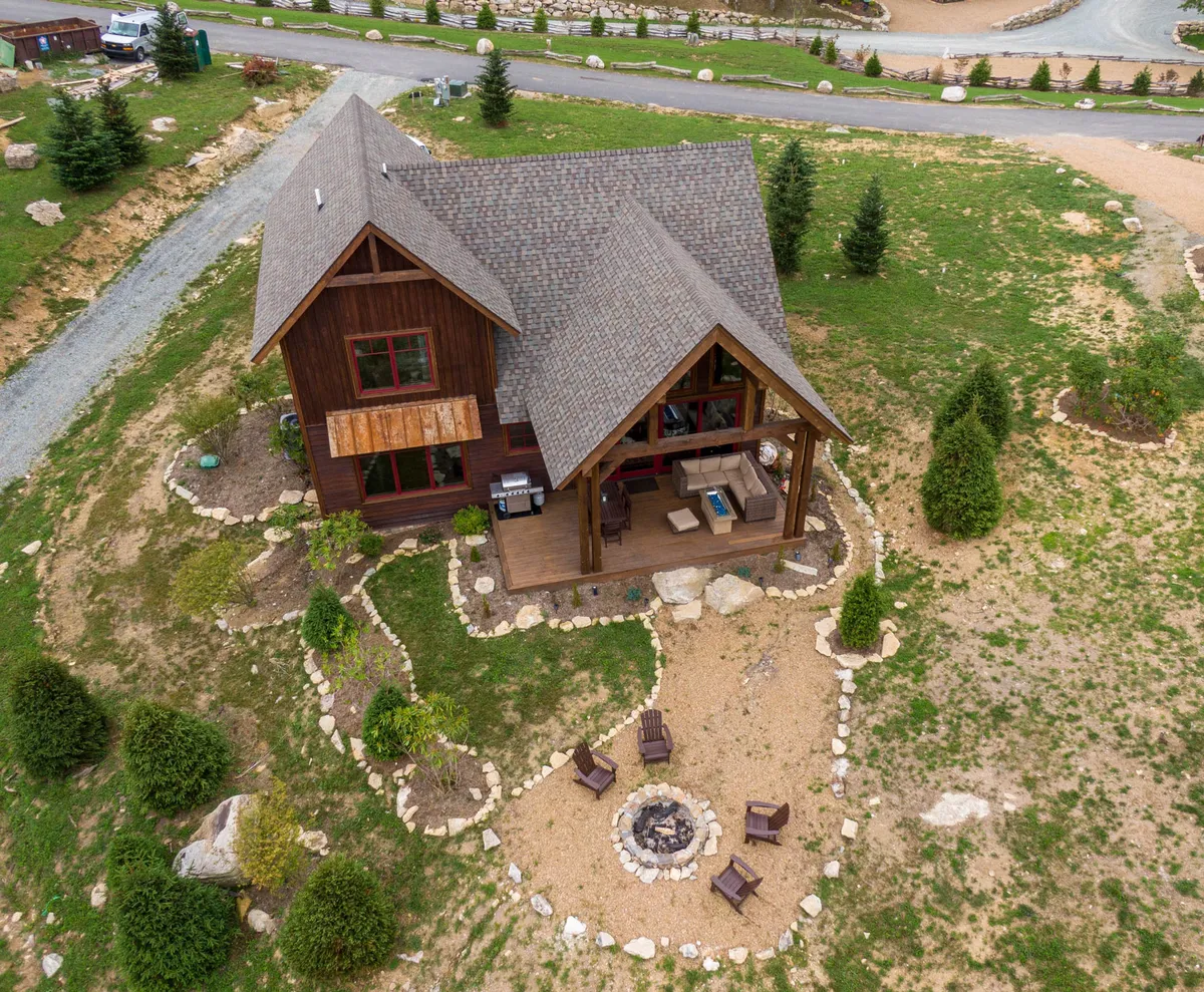 A welcoming exterior view of the house features a charming wooden façade, an inviting fire pit area, and a landscaped garden. The scene suggests communal outdoor spaces perfect for sunset gatherings, stargazing, and shared moments, all surrounded by natural beauty.