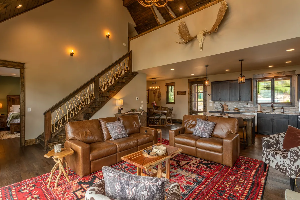An inviting living area with leather sofas, a rustic coffee table, a colorful area rug, a wooden staircase, and a chandelier with antlers. The scene feels lively and perfect for gatherings, celebrations, and creating lasting memories.