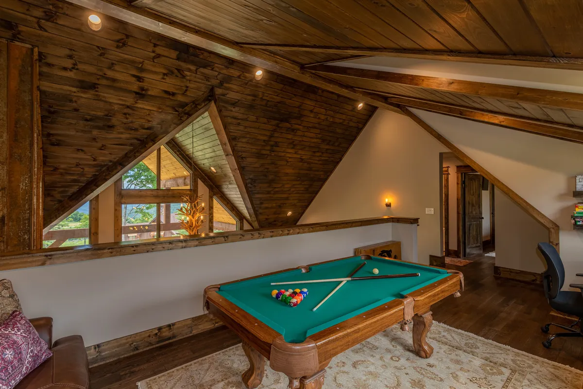 A spacious loft area featuring a pool table at the center, surrounded by exposed wooden beams and decorative plants. The casual atmosphere encourages relaxation and entertainment, perfect for game nights and family fun.